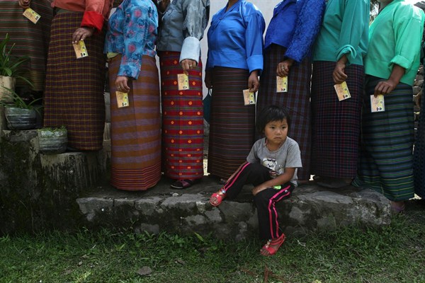 A Bhutanese child sits as adults in traditional costume stand in a queue to cast their votes for the nation’s parliamentary election outside a polling station at Rikhey, Bhutan, April 23, 2013 (AP photo by Anupam Nath).