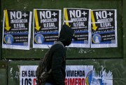 A migrant walks past anti-immigration posters that read in Spanish “No more illegal immigration. Solidarity begins at home,” Santiago, Chile, Aug. 20, 2017 (AP photo by Esteban Felix).