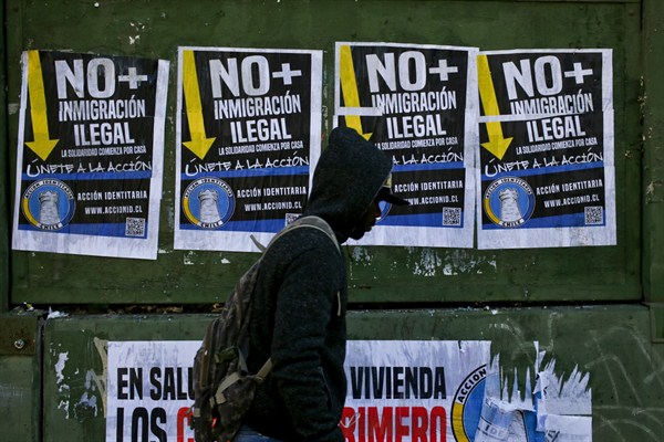 A migrant walks past anti-immigration posters that read in Spanish “No more illegal immigration. Solidarity begins at home,” Santiago, Chile, Aug. 20, 2017 (AP photo by Esteban Felix).