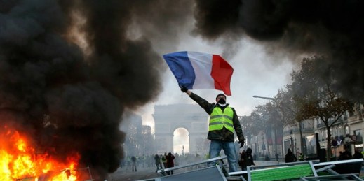 A demonstrator waves the French flag near a burning barricade on the Champs Elysees, Paris, Nov. 24, 2018 (AP photo by Michel Euler).