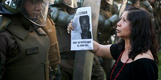 A woman shows a picture of Mapuche indigenous man Camilo Catrillanca, who was killed by security forces, to riot police during a protest in Santiago, Chile, Nov. 19, 2018 (AP photo by Esteban Felix).