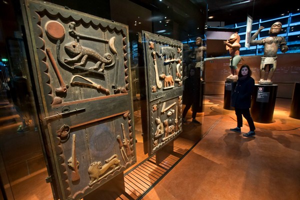 A visitor walks past a door of a palace from the Kingdom of Dahomey in present-day Benin, on display in the Quai Branly museum, Paris, Nov. 23, 2018 (AP photo by Michel Euler).
