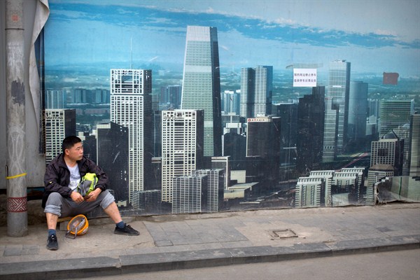 A worker sits in front of a billboard at a construction site in Beijing, China, May 16, 2019 (AP photo by Mark Schiefelbein).