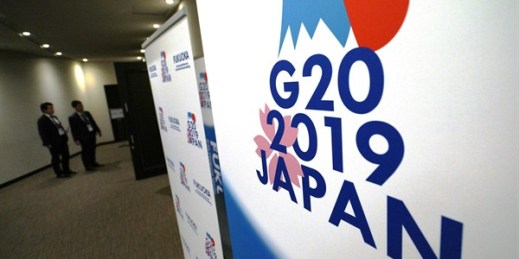 Staff members stand near the emblem for the 2019 Group of 20 leaders’ summit at the entrance of the press center of the G-20 Finance Ministers’ and Central Bank Governors’ meeting, in Fukuoka, Japan, June 9, 2019 (AP photo by Eugene Hoshiko).