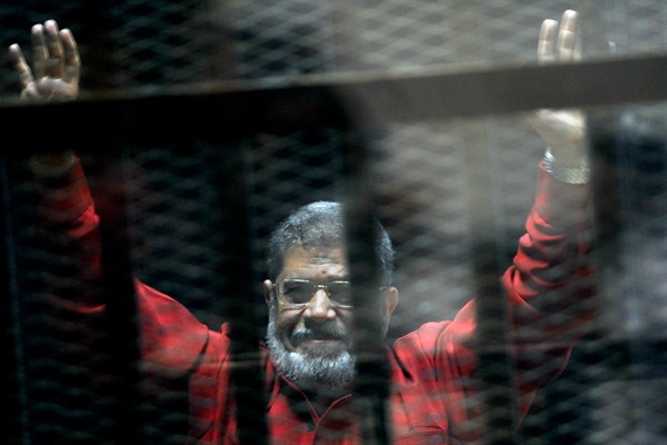 Former Egyptian President Mohammed Morsi raises his hands inside a defendant’s cage in a makeshift courtroom at the national police academy, in an eastern suburb of Cairo, Egypt, June 21, 2015 (AP photo by Ahmed Omar).