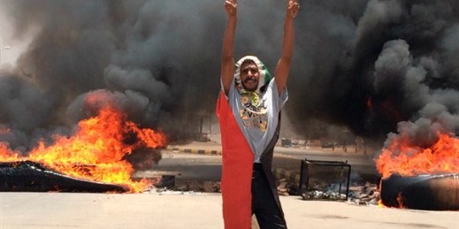 A protester flashes the victory sign in front of burning tires and debris near the military’s headquarters, Khartoum, Sudan, June 3, 2019 (AP photo).