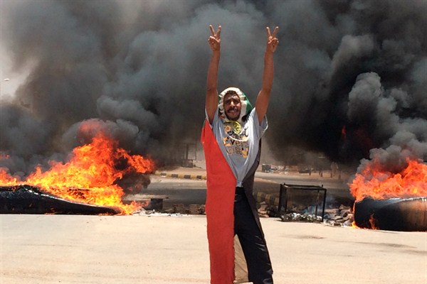 A protester flashes the victory sign in front of burning tires and debris near the military’s headquarters, Khartoum, Sudan, June 3, 2019 (AP photo).