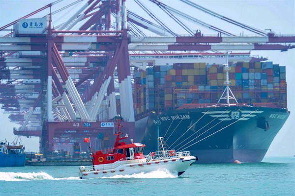 A boat sails past a cargo ship at a port in Qingdao, Shandong province, China, June 10, 2019 (Chinatopix photo via AP Images).