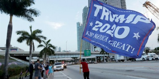 A supporter of President Donald Trump carries a flag outside of the venue for the Democratic presidential primary debate, in Miami, June 26, 2019 (AP photo by Lynne Sladky).