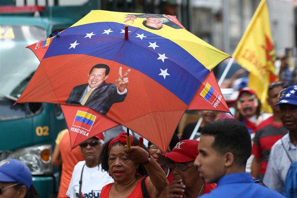 A supporter of Venezuelan President Nicolas Maduro wears a parasol in the colors of the Venezuelan flag and with the picture of the late Hugo Chavez, at a pro-government rally in Caracas, May 20, 2019 (DPA photo by Pedro Mattey via AP).