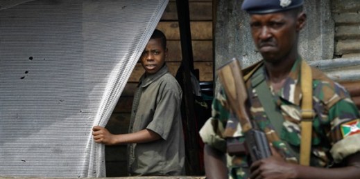A young boy and a soldier watch demonstrators climb onto a container used as a barricade in the Cibitoke neighborhood of Bujumbura, Burundi, May 19, 2015 (AP photo by Jerome Delay).