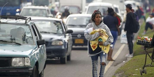 A Venezuelan migrant, cradling a baby, walks along a street in Bogota, Colombia, April 4, 2019 (AP photo by Fernando Vergara).
