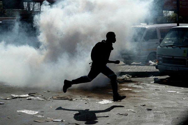 A man runs away from tear gas after making off with goods from a store in Germiston, east of Johannesburg, South Africa, Sept. 3, 2019 (AP photo by Themba Hadebe).
