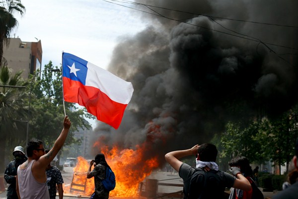 An anti-government protester waves a Chilean flag during clashes with police amid a general strike in Santiago, Chile, Oct. 23, 2019 (AP photo by Luis Hidalgo).