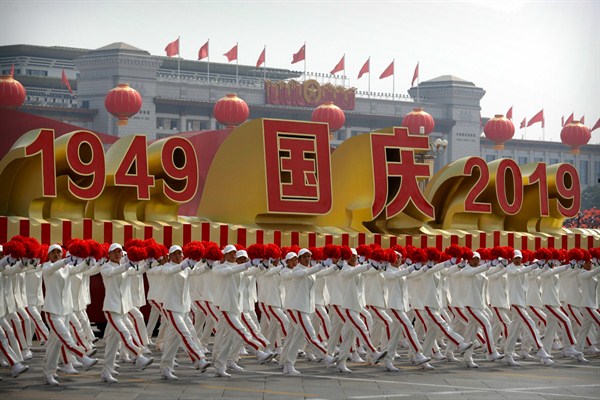 Parade participants wave flowers as they march next to a float commemorating the 70th anniversary of the founding of the People’s Republic of China, Beijing, Oct. 1, 2019 (AP photo by Mark Schiefelbein).