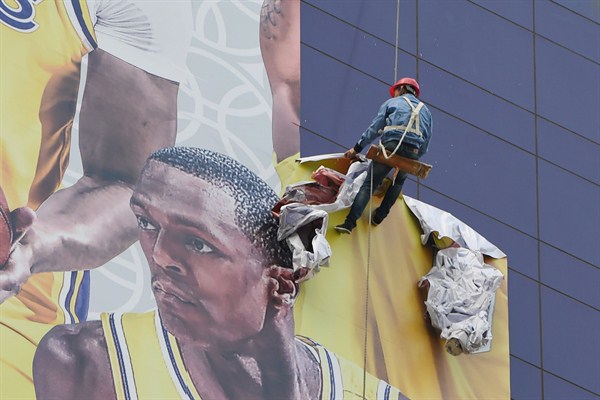 A worker tears down a poster promoting a game between the Los Angeles Lakers and Brooklyn Nets in Shanghai, China, Oct. 9, 2019 (Photo by Yu Zhongyue for Imaginechina via AP Images).