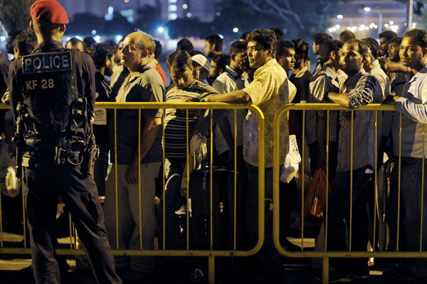 A police officer watches over migrant workers as they wait for shuttle buses to take them back to their dormitories, Singapore, Feb. 9, 2014 (AP photo by Joseph Nair).