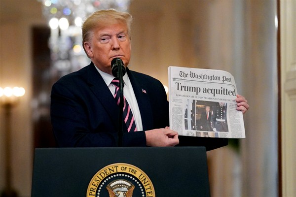 President Donald Trump holds up a newspaper with a headline that reads “Trump acquitted” during an event in the East Room of the White House, Washington, Feb. 6, 2020 (AP photo by Evan Vucci).