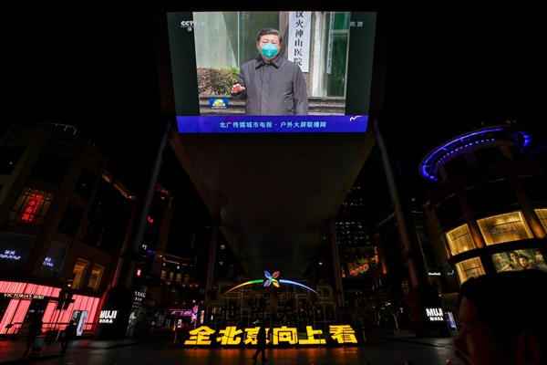 People walk by a giant TV screen at a shopping mall in Beijing showing China’s leader, Xi Jinping, talking to medical workers as he visited a hospital in Wuhan, March 10, 2020 (AP photo by Andy Wong).
