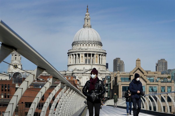 People wear masks as they walk over Millennium Bridge near St Paul’s Cathedral, in London, March 22, 2020 (AP photo by Kirsty Wigglesworth).