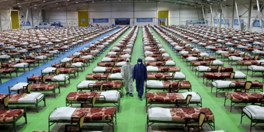 People in protective clothing walk past rows of beds at a temporary 2,000-bed hospital for COVID-19 patients in Tehran, Iran, March 26, 2020 (AP photo by Ebrahim Noroozi).