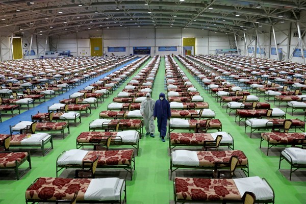 People in protective clothing walk past rows of beds at a temporary 2,000-bed hospital for COVID-19 patients in Tehran, Iran, March 26, 2020 (AP photo by Ebrahim Noroozi).