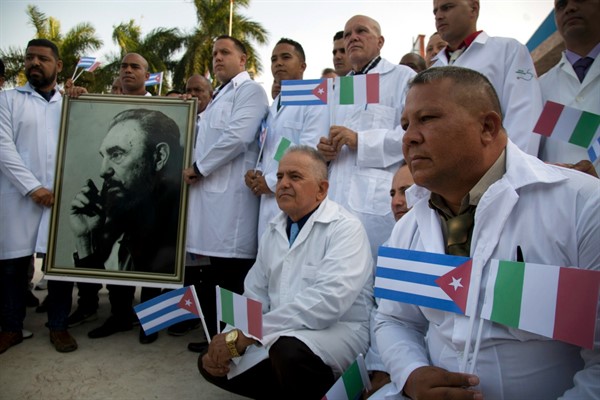 Cuban doctors and medical professionals pose with a photo of Fidel Castro before departing for Italy to assist with the coronavirus outbreak in the country, Havana, Cuba, March 21, 2020 (AP photo by Ismael Francisco).
