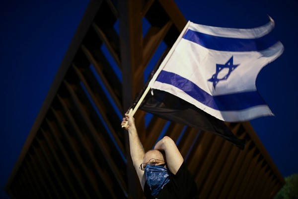 A protester waves the Israeli national flag during a demonstration against Prime Minister Benjamin Netanyahu, Tel Aviv, Israel, April 19, 2020 (AP photo by Oded Balilty).