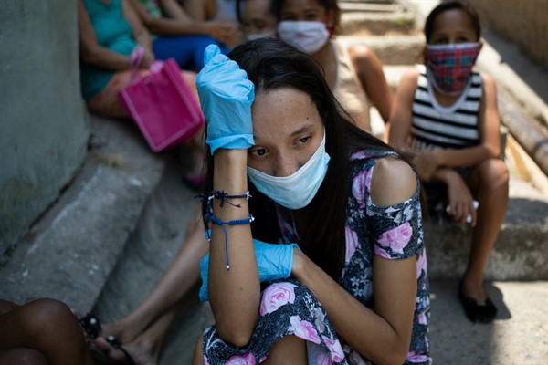A woman wearing a mask and gloves waits outside a soup kitchen run by nuns in Caracas, Venezuela, April 30, 2020 (AP photo by Ariana Cubillos).
