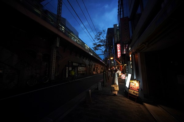 A woman wearing a face mask looks at a menu of a restaurant on an empty street in Tokyo, April 28, 2020. (AP photo by Eugene Hoshiko).