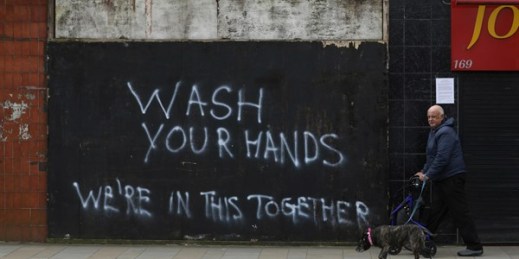 A man walks his dog past graffiti calling for people to wash their hands in Belfast, Northern Ireland, March 30, 2020 (AP photo by Peter Morrison).