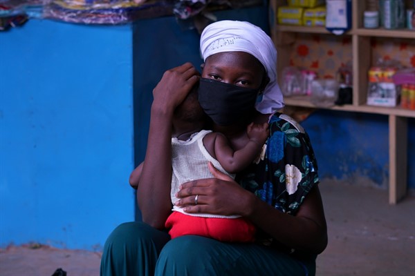 A woman wearing a face mask holds her child at a marketplace in the Nioko-2 suburb of Ouagadougou, Burkina Faso, May 14, 2020 (photo courtesy of Clair MacDougall).