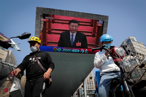 Food delivery workers near a TV screen showing Chinese leader Xi Jinping attending the closing ceremony of the National People’s Congress, in Beijing, China, May 28, 2020 (AP photo by Andy Wong).