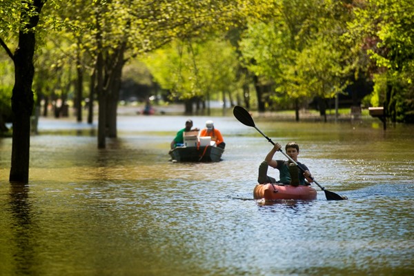 A boy paddles a kayak down a flooded street in Midland, Mich., May 20, 2020 (Photo by Katy Kildee for Midland Daily News via AP Images).