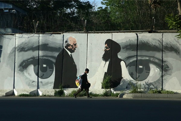 A young boy walks past a mural depicting the U.S. peace envoy, Zalmay Khalilzad, left, and Mullah Abdul Ghani Baradar, the leader of the Taliban delegation, in Kabul, Afghanistan, May 5, 2020 (AP Photo by Rahmat Gul).
