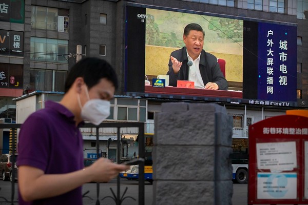 A man walks past a large video screen showing Chinese leader Xi Jinping speaking in Beijing, June 30, 2020 (AP photo by Mark Schiefelbein).