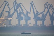 A fishing boat sails near the cranes of Cao Feidian Port in Tangshan, China, Feb. 20, 2012 (AP photo by Alexander F. Yuan).