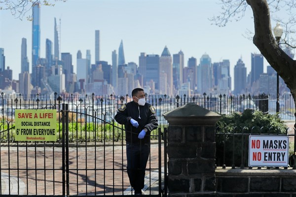 A security guard stands behind the gates of a temporarily closed park with a view of the New York City skyline, in Weehawken, N.J., April 28, 2020 (AP photo by Seth Wenig).