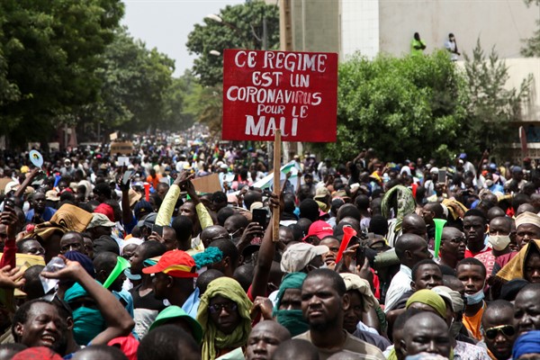 Demonstrators hold a placard in French reading, “This regime is a coronavirus for Mali,” as they protest in, Bamako, Mali, June 5, 2020 (AP photo by Baba Ahmed).