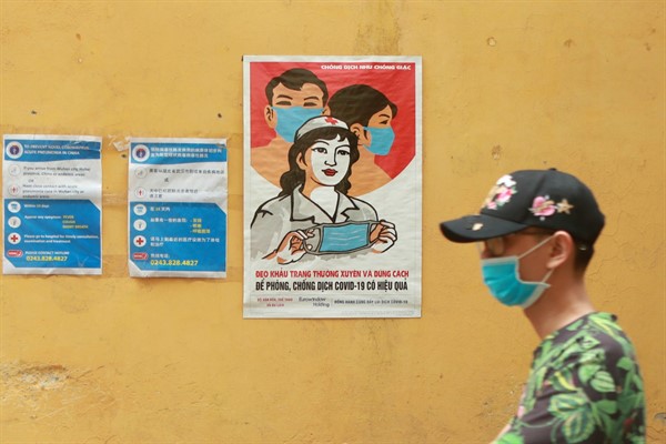 A man walks past a poster encouraging people to wear face masks correctly in Hanoi, Vietnam, Apr. 23, 2020 (AP photo by Hau Dinh).