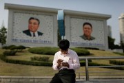 A man uses his smartphone in front of portraits of the late North Korean leaders Kim Il Sung, left, and Kim Jong Il, right, in Pyongyang, May 5, 2015 (AP photo by Wong Maye-E).
