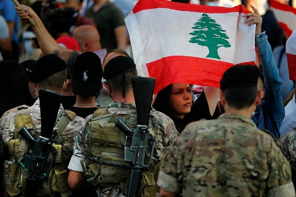 An anti-government protester holds a national flag in front of Lebanese army soldiers during a protest in Zalka, Lebanon, Oct. 5, 2020 (AP photo by Hussein Malla).