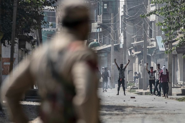 A police officer watches Kashmiri men protest following a shootout between police and militants, Srinagar, India, Sept. 17, 2020 (AP photo by Mukhtar Khan).