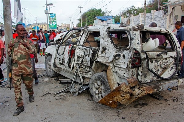 A member of the security forces walks past a wrecked vehicle outside the Elite Hotel following an al-Shabab attack, in Mogadishu, Somalia, Aug. 17, 2020 (AP photo by Farah Abdi Warsameh).