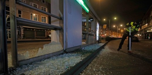A police officer sweeps up glass from a bus stop that was smashed during protests against a nationwide curfew in Rotterdam, Netherlands, Jan. 25, 2021 (AP photo by Peter Dejong).