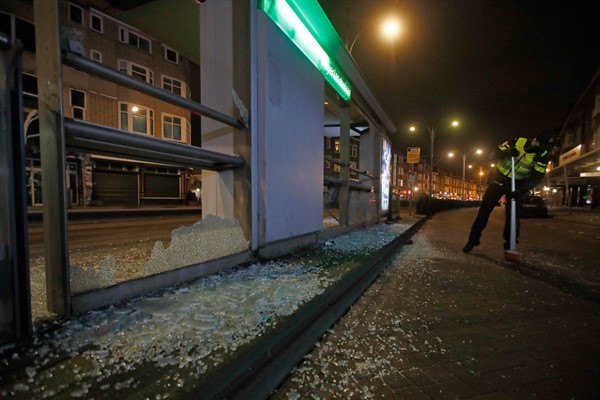 A police officer sweeps up glass from a bus stop that was smashed during protests against a nationwide curfew in Rotterdam, Netherlands, Jan. 25, 2021 (AP photo by Peter Dejong).