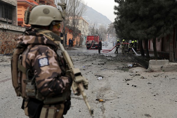 A soldier stands guard as firefighters work at the site of a bomb attack in Kabul, Afghanistan, Feb. 20, 2021 (AP photo by Rahmat Gul).