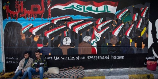 Two protesters sit by a mural with Arabic that reads, “Iraq,” in Tahrir Square, Baghdad, Jan. 8, 2020 (AP photo by Nasser Nasser).