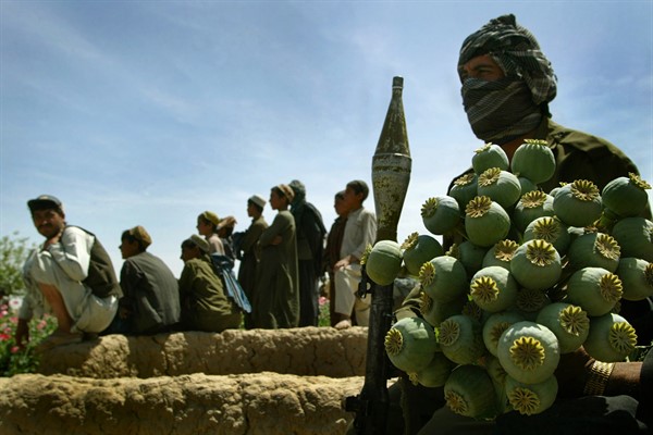 Armed Afghan policemen sit with confiscated poppy bulbs during a poppy eradication sweep of a farmer’s field in the village of Karezaq, Afghanistan, April 11, 2004 (AP photo by David Guttenfelder).