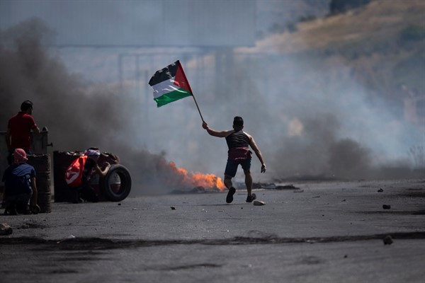 A protester waves the Palestinian flag during clashes with the Israeli forces at the Hawara checkpoint, south of the West Bank city of Nablus, May 14, 2021 (AP photo by Majdi Mohammed).